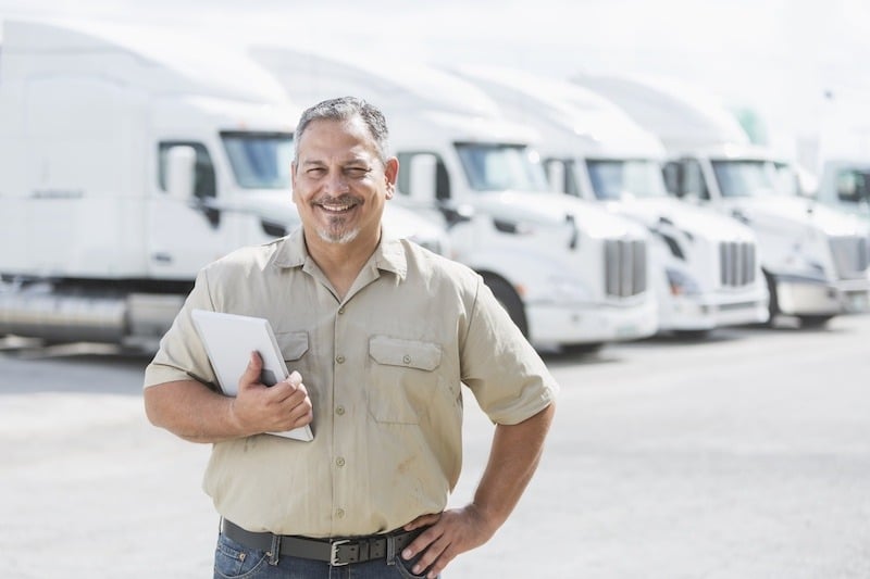 Truck Driver Posing for a Photo in a Truck Yard With Trucks in the Background