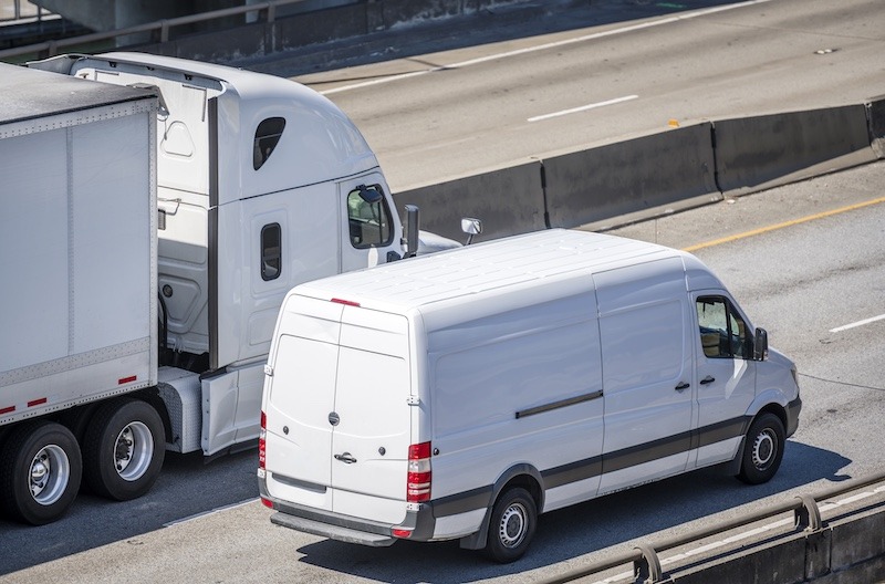 A White Freight Truck and White Delivery Van Driving Down the Highway